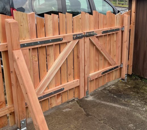 Holz-Gartentor mit diagonalen Verstrebungen, teilweise offen, neben einem Auto.